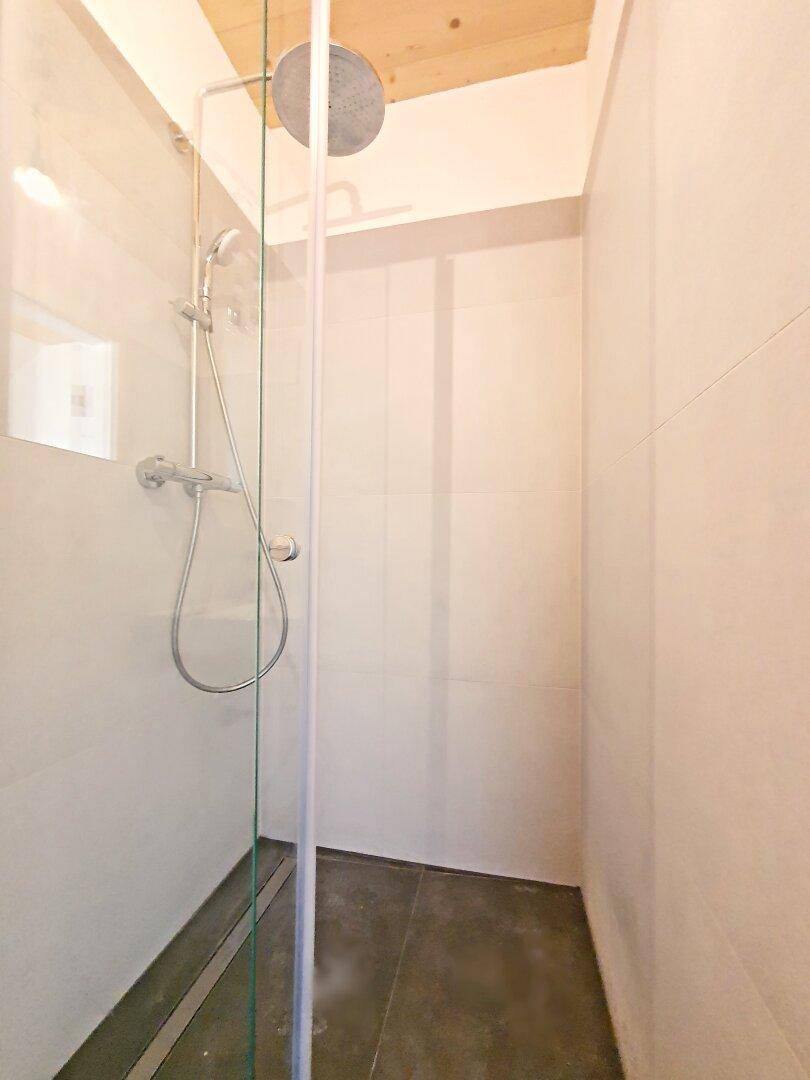 Moderne Duschkabine mit Regenduschkopf und grauen Fliesen.