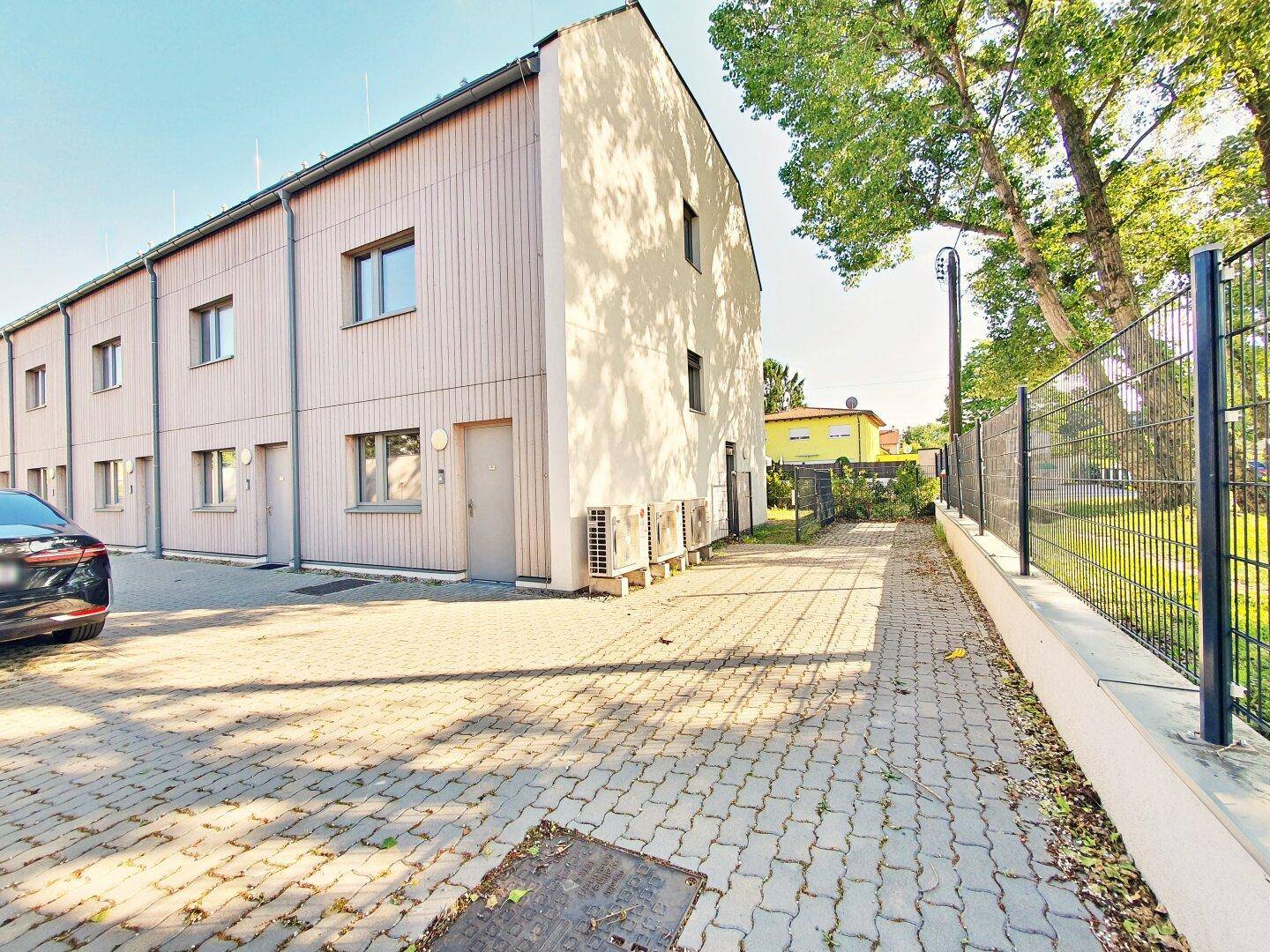 Reihenhausfassade mit Parkplätzen und angrenzendem Grünbereich.