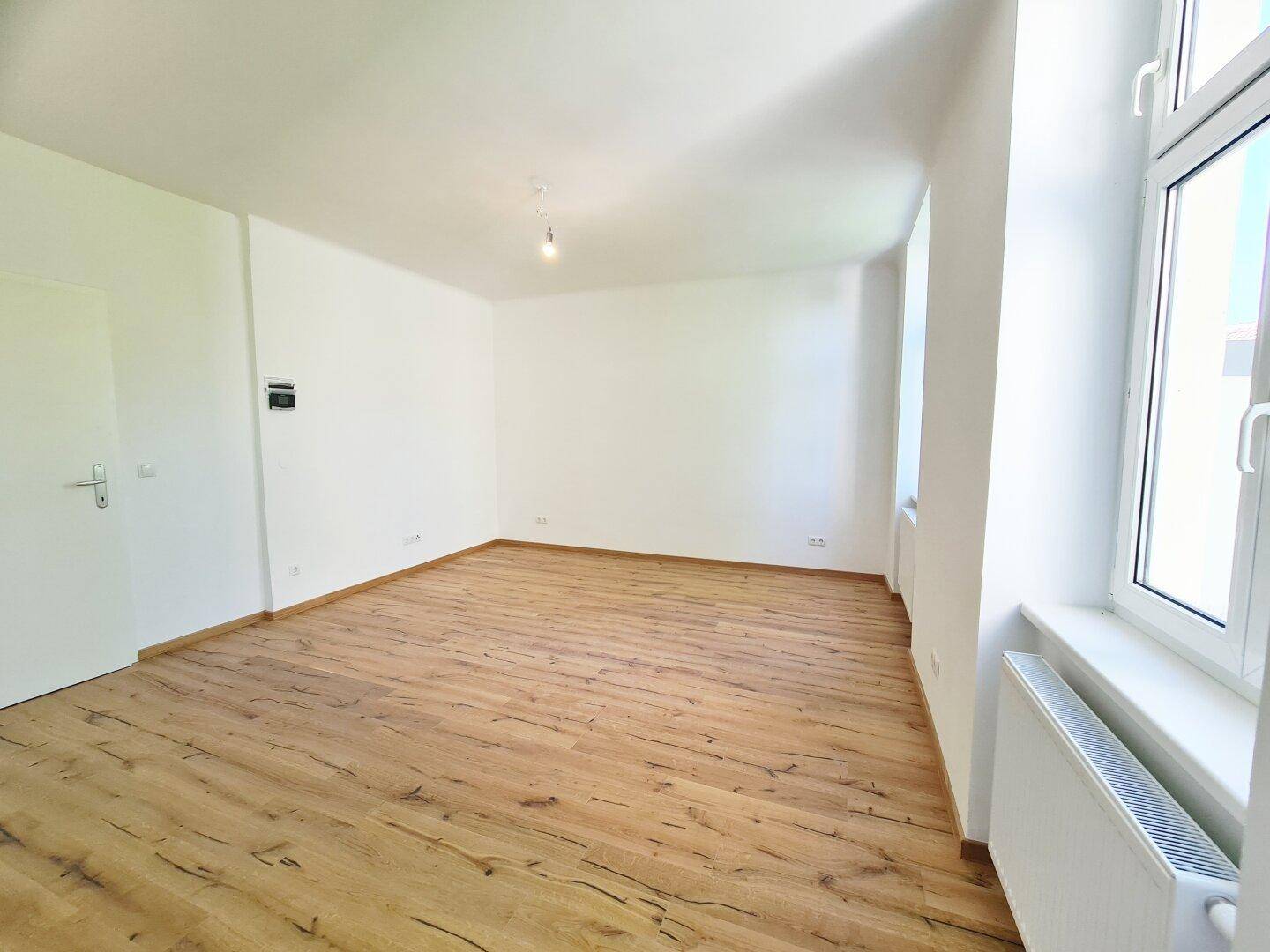 Helles, leeres Zimmer mit neuem Laminatboden und weißen Wänden, bereit zum Einzug.