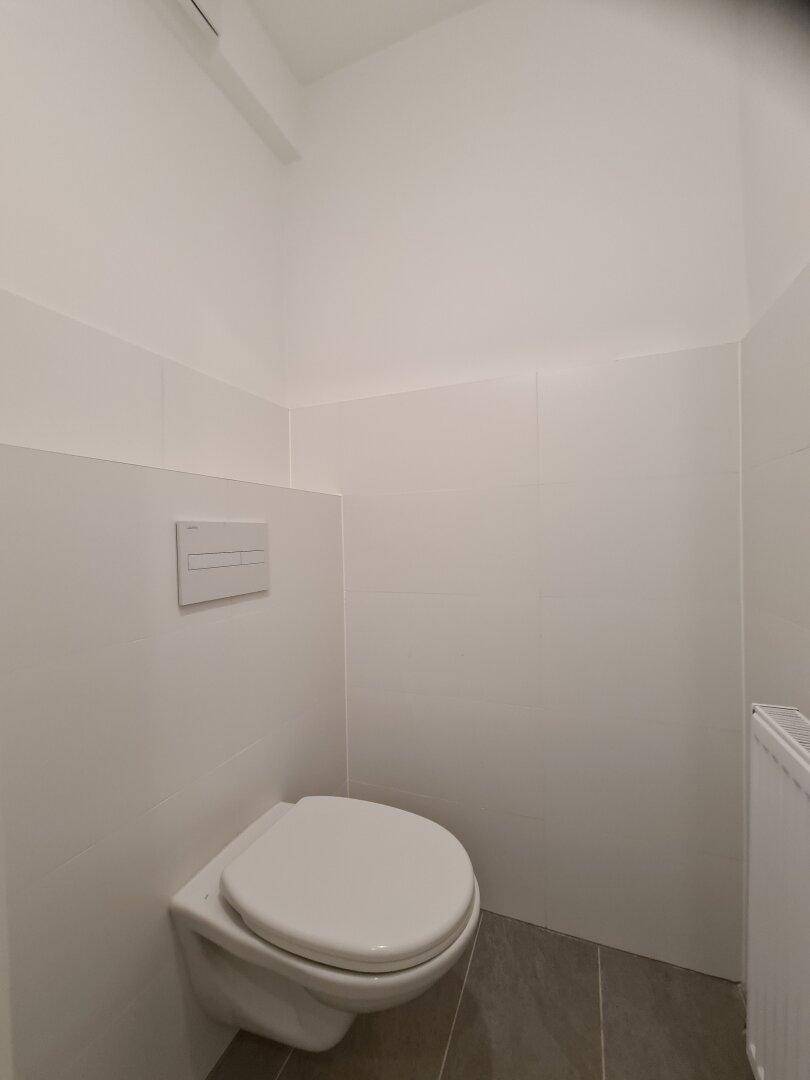 Sauberes WC mit wandhängender Toilette und weißen Fliesen an den Wänden.