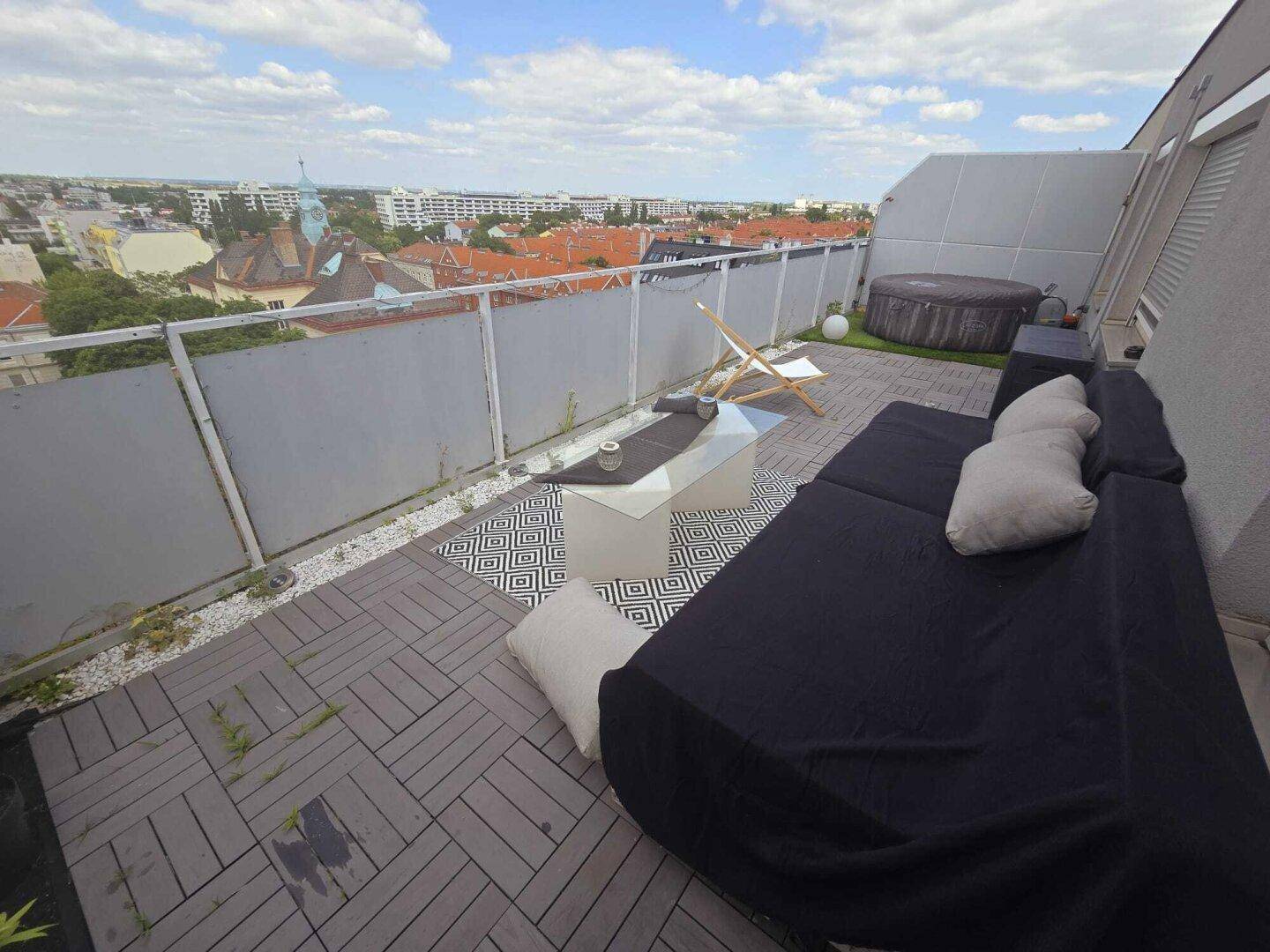 Dachterrasse mit Lounge-Möbeln, Couchtisch und einem Whirlpool im Hintergrund.