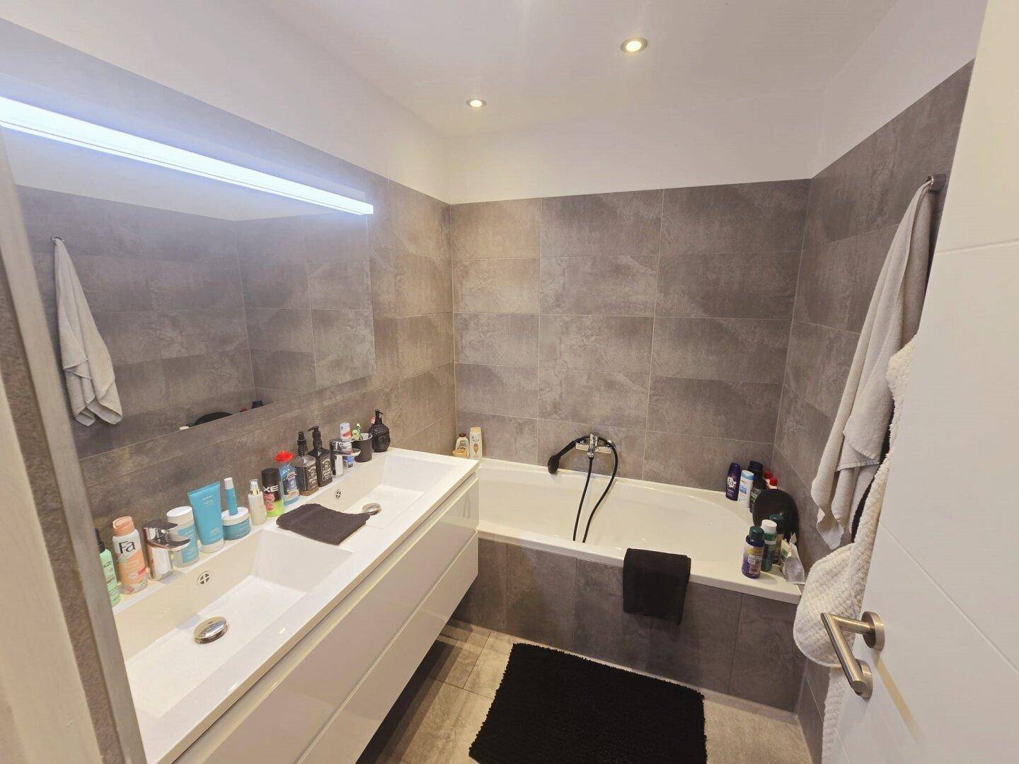 Modernes Badezimmer mit Doppelwaschbecken, Badewanne und großformatigen grauen Fliesen.