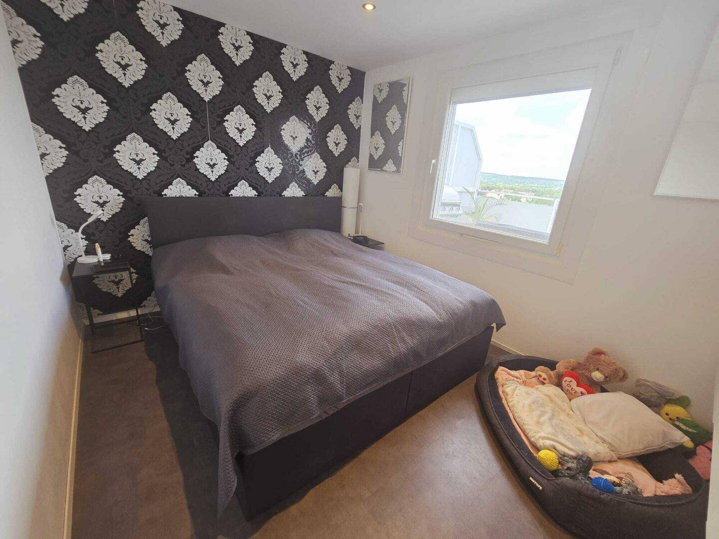 Schlafzimmer mit großem Bett, gemusterter Tapete und einem Fenster mit Ausblick.