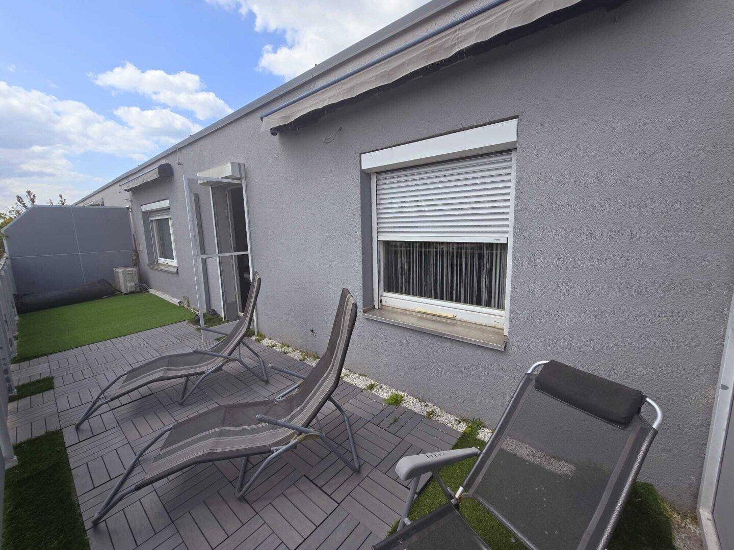 Teil der Dachterrasse mit Liegestühlen, Kunstrasen und Blick auf die Gebäudefassade.