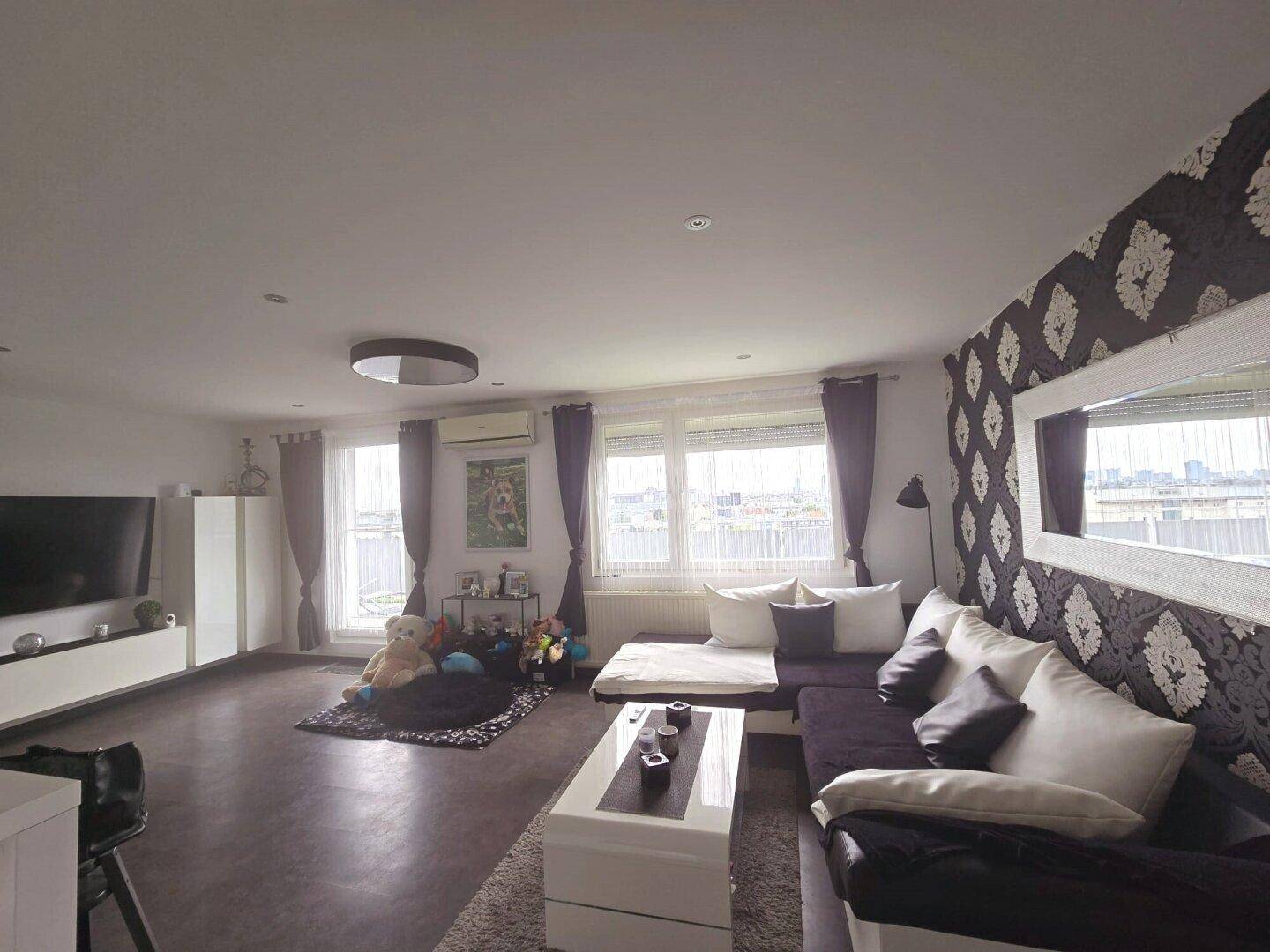 Geräumiges Wohnzimmer mit großem Sofa, Fernseher und dekorativer Tapete, hell durch große Fenster.