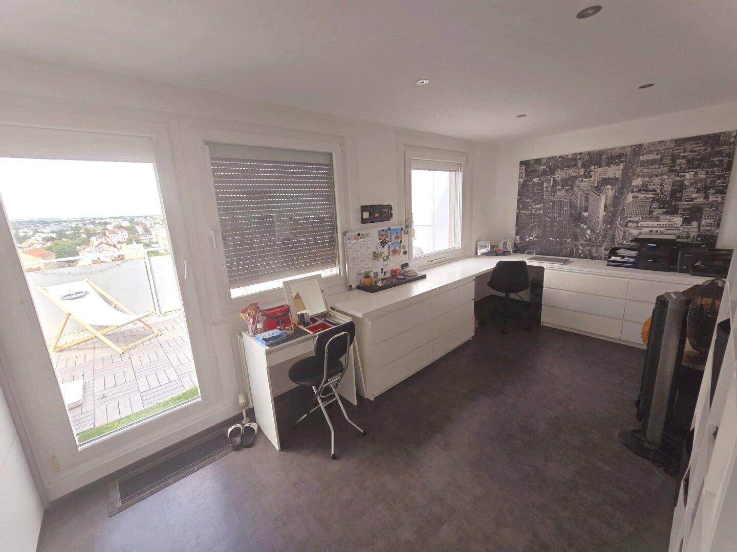 Helles Arbeitszimmer mit langem Schreibtisch, Stauraum und Zugang zur Dachterrasse mit Stadtblick.