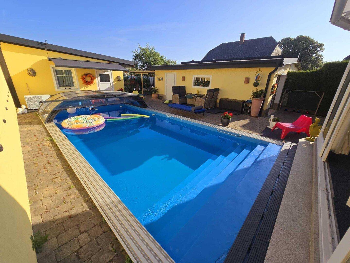 Außenbereich mit großem, blauem Pool und gepflasterter Terrasse unter strahlendem Himmel.