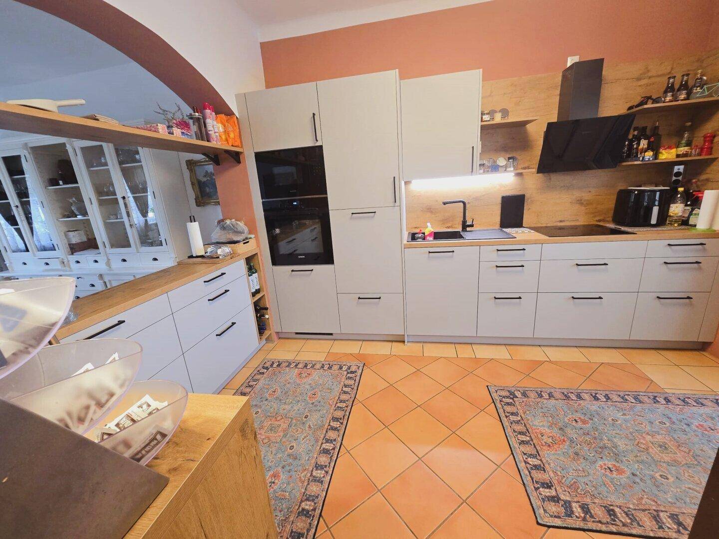 Moderne Küche mit hellgrauen Fronten, Holzarbeitsplatten und integrierten Geräten.