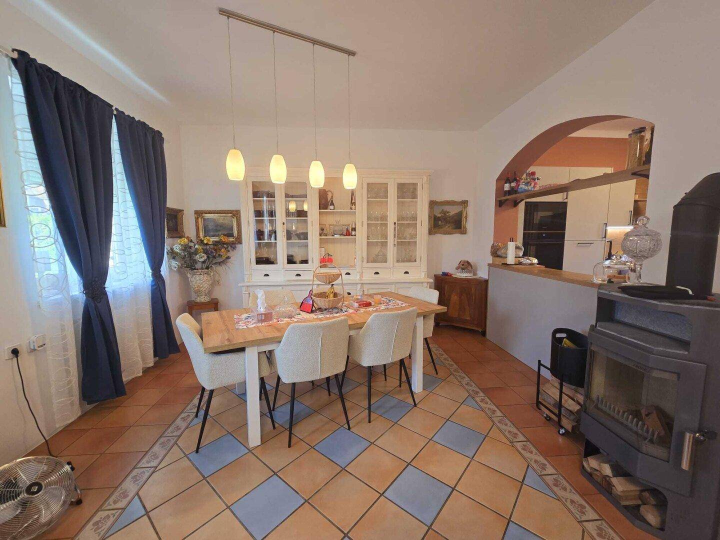 Gemütlicher Wohn-Essbereich mit Holztisch, Kaminofen und traditionellen Fliesenböden.
