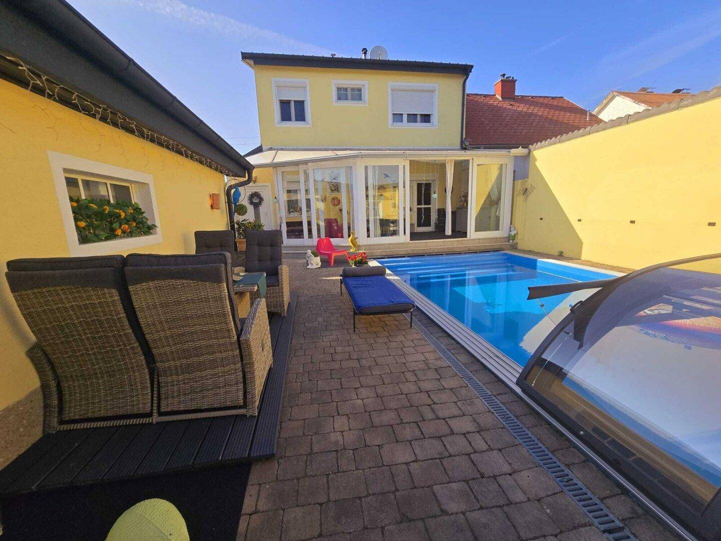 Ansicht des Hauses mit Wintergarten, Poolbereich und gepflastertem Hof.