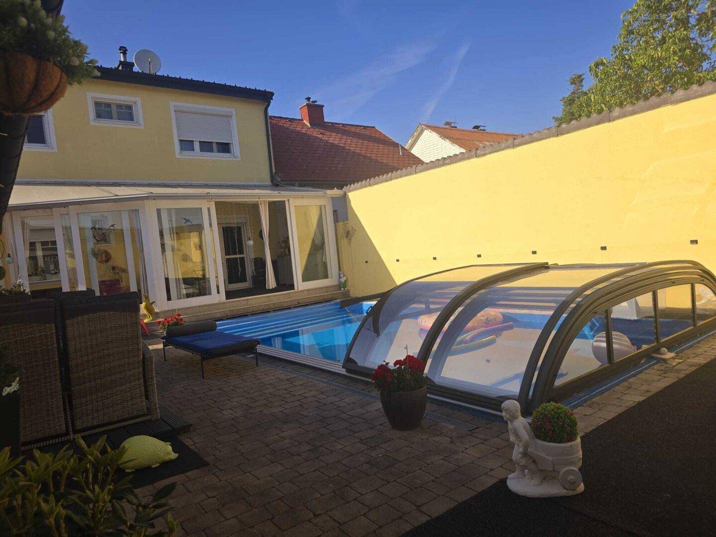 Rückansicht des Hauses mit Poolabdeckung und sonnigem Außenbereich.