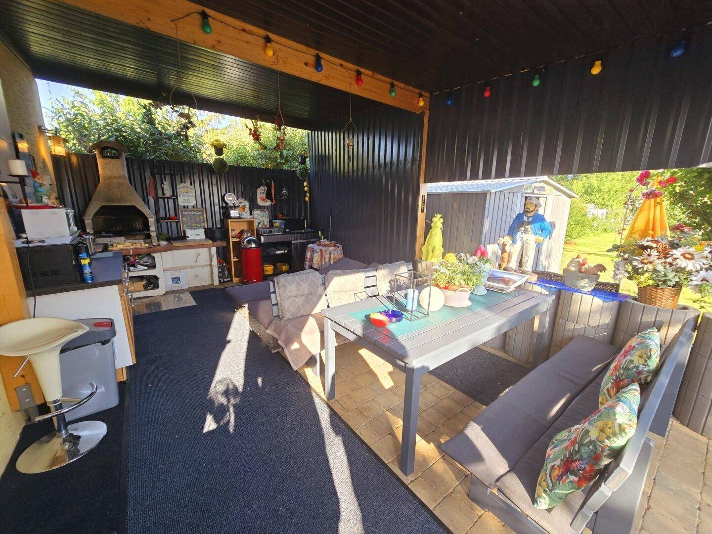 Überdachte Terrasse mit Sitzgelegenheiten, Außenküche und Grillbereich, ideal für gesellige Abende.