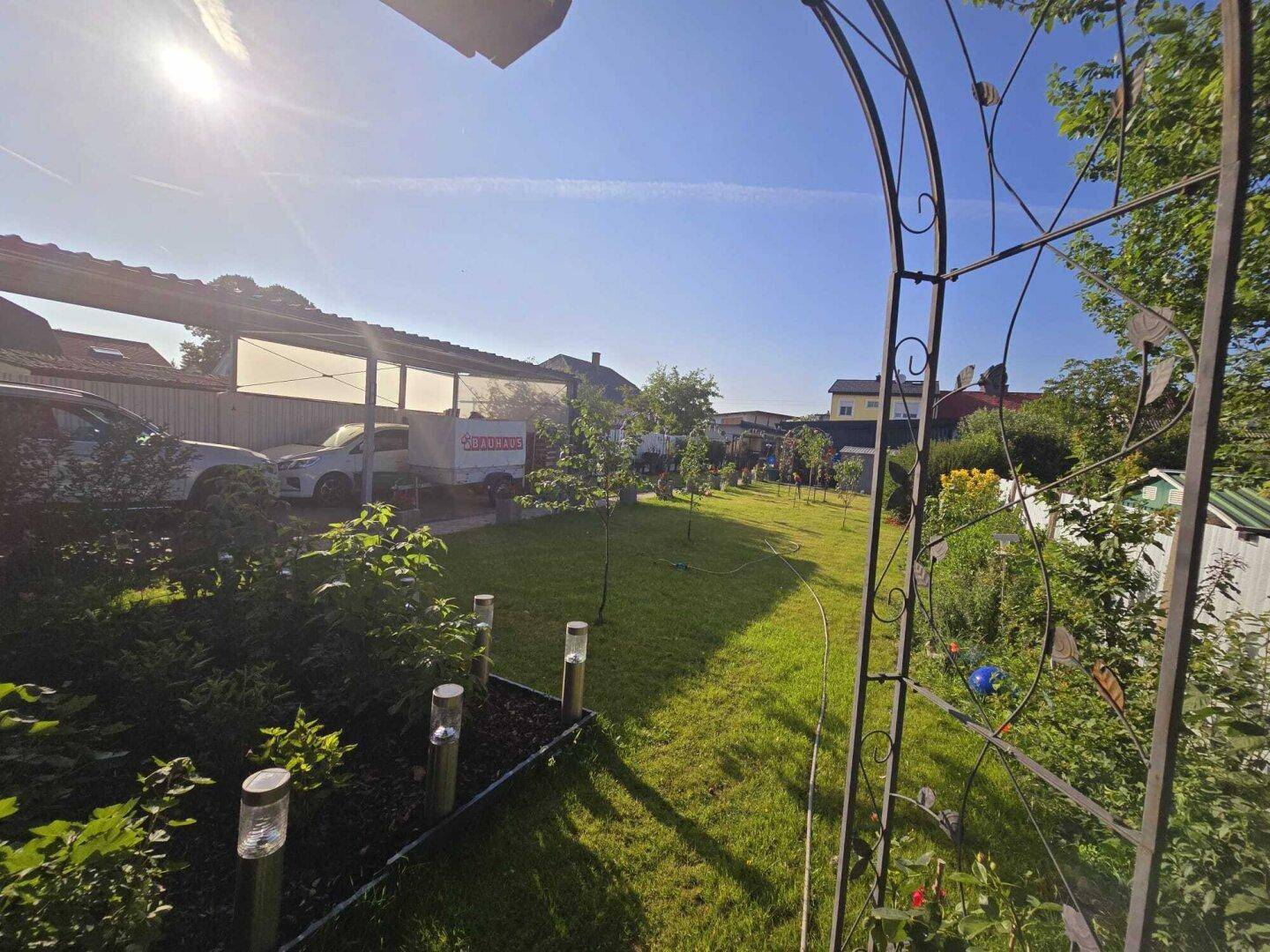Weitläufiger Garten mit Rasen, Bäumen und einem Carport im Hintergrund.
