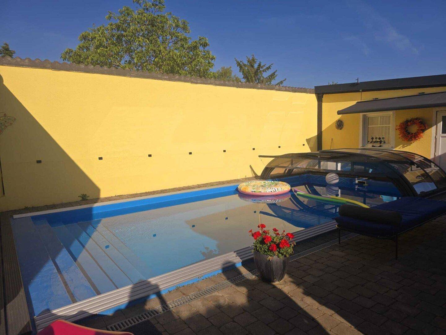 Sonnige Poollandschaft mit gepflastertem Bereich und hoher Mauer für Privatsphäre.