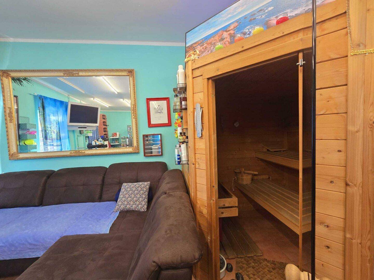 Wohnbereich mit integrierter Holzsauna, großem Sofa und Spiegel, ideal zur Entspannung.