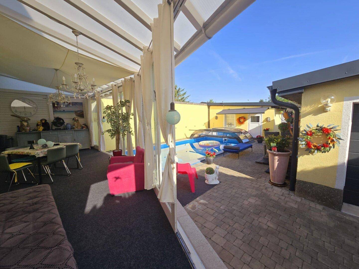 Geräumiger Wintergarten mit Essbereich, Blick auf den Pool und viel Tageslicht.