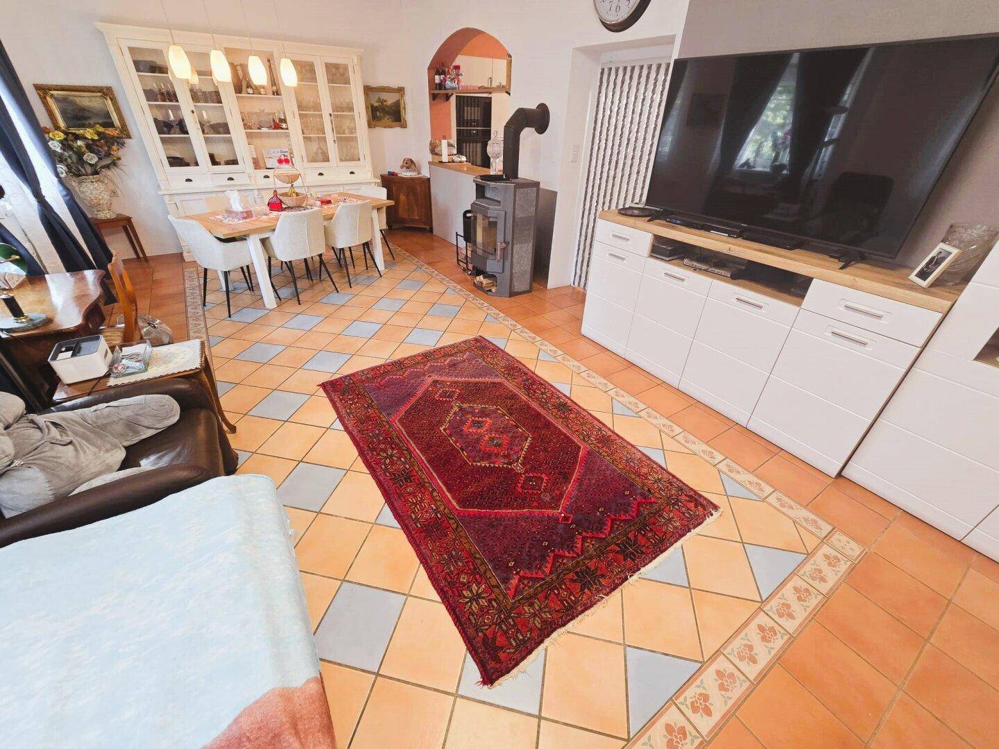 Gemütliches Wohnzimmer mit großem Fernseher, Teppich und Fliesenboden.