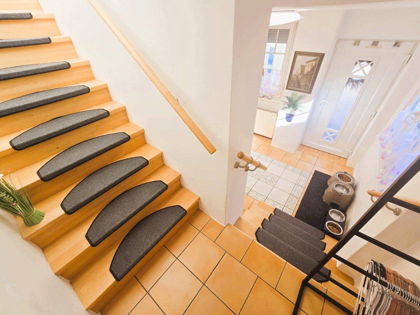 Heller Eingangsbereich mit Holztreppe und Fliesenboden, führt zu den oberen Etagen.
