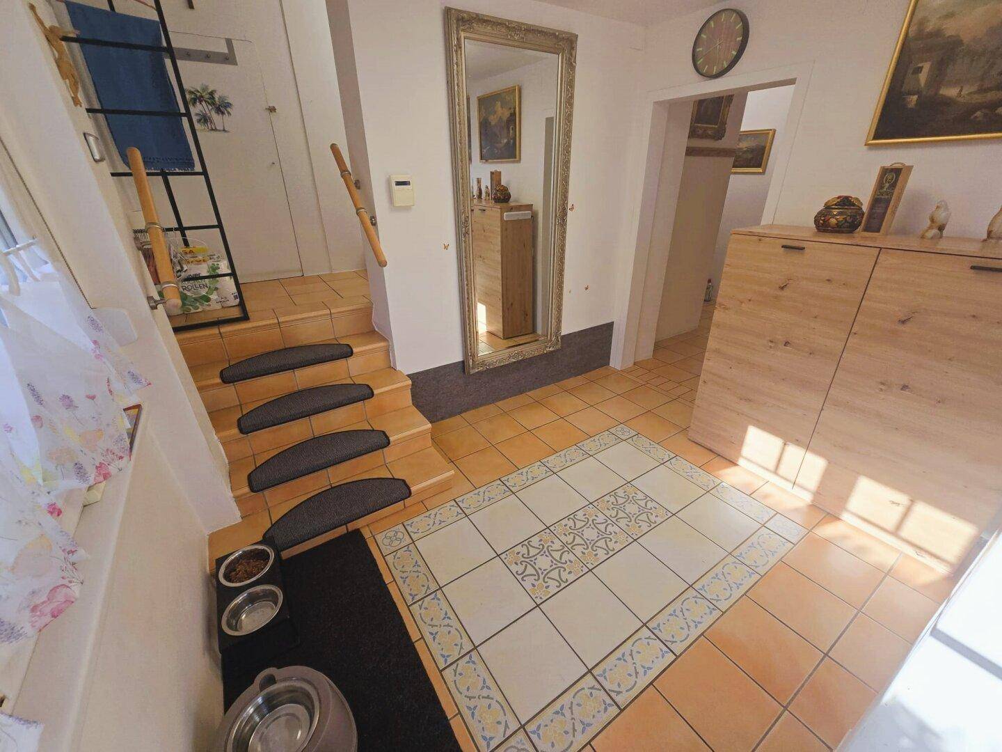 Geräumiger Eingangsbereich mit Fliesenboden, großem Spiegel und Treppe, hell und einladend.