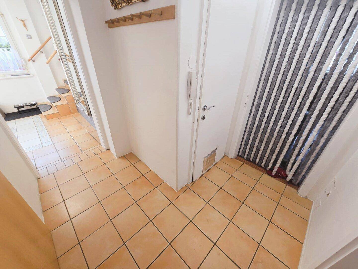 Heller Flur mit Terrakotta-Fliesenboden, der zu verschiedenen Räumen und einer Treppe führt.