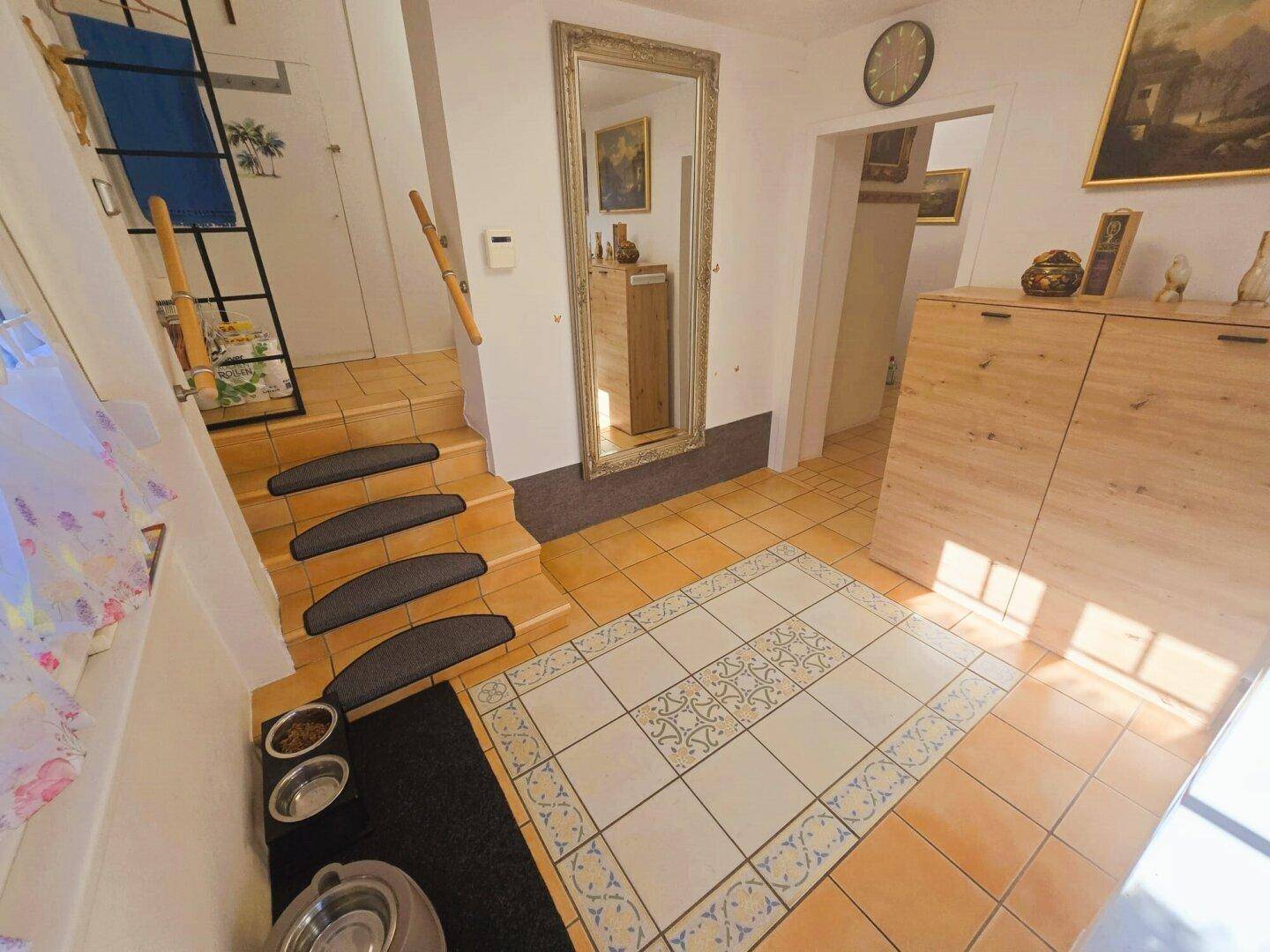 Geräumiger Eingangsbereich mit Fliesenboden, großem Spiegel und Treppe, hell und einladend.
