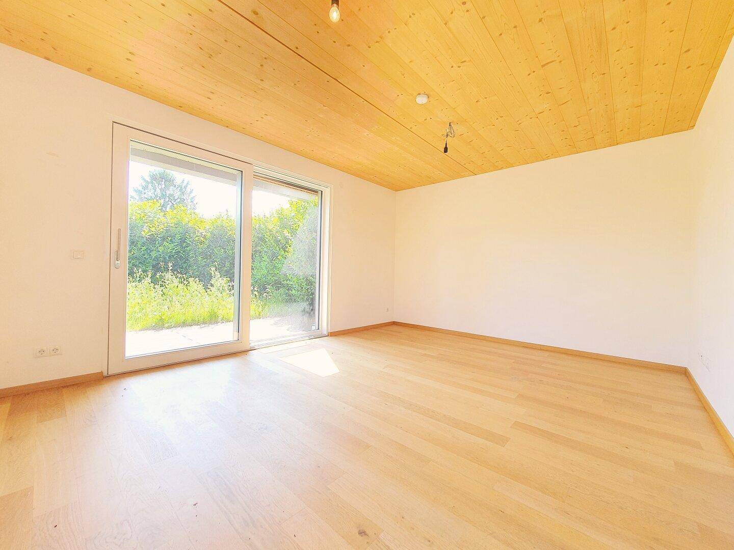 Heller Raum mit Holzdecke, Holzboden und großer Schiebetür mit Blick ins Grüne.
