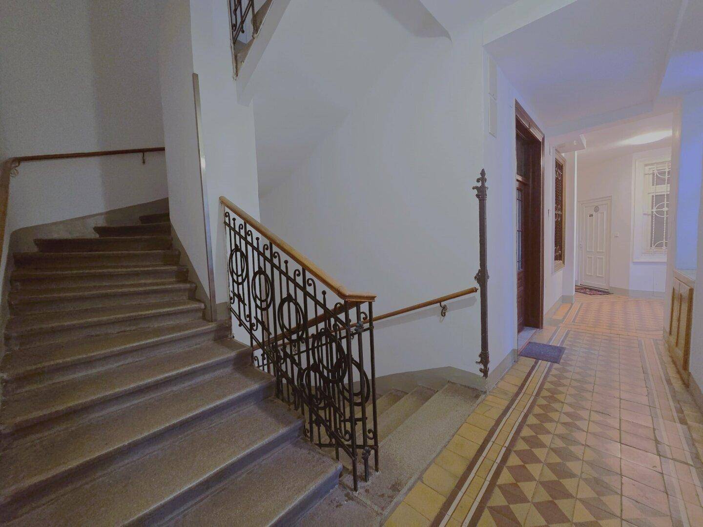 Treppenhaus mit kunstvollem Metallgeländer und gemustertem Fliesenboden im Eingangsbereich.