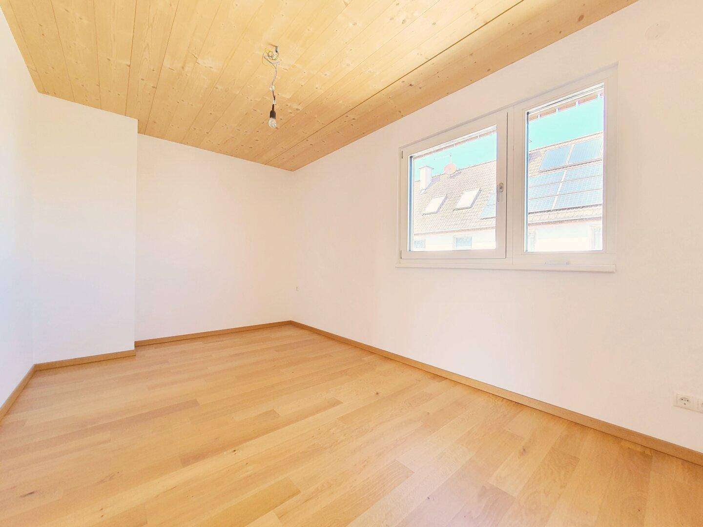 Schlafzimmer mit Parkettboden, Holzbalkendecke und Fenster mit Blick auf Dächer.