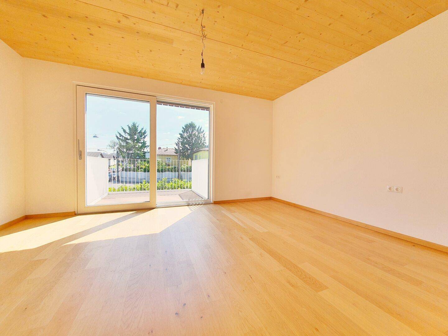 Helles Schlafzimmer mit Parkettboden, Holzbalkendecke und Zugang zum Balkon.