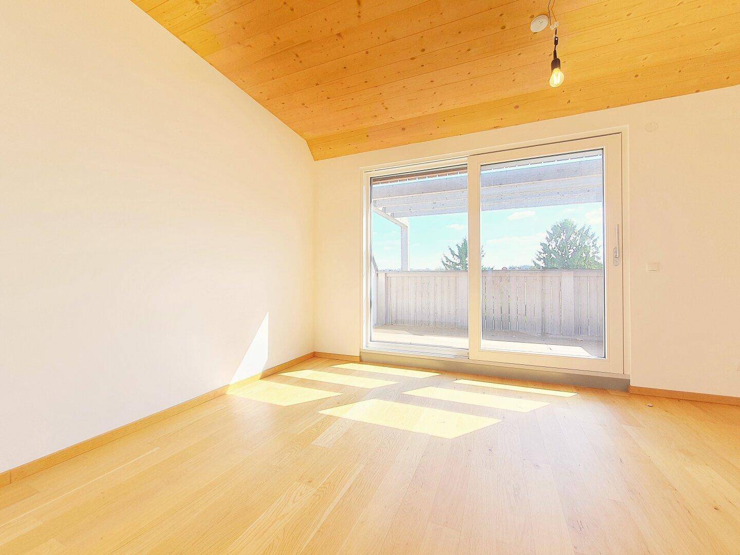 Helles Schlafzimmer mit Parkettboden, Holzbalkendecke und Zugang zum Balkon.