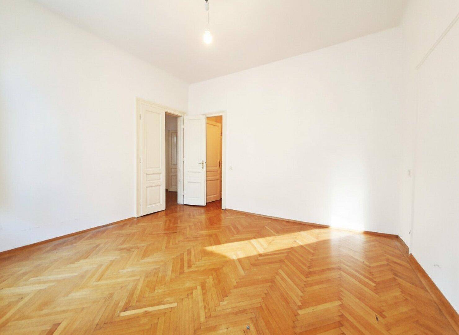 Heller Raum mit Fischgrätparkett und zwei Türen, die zu anderen Bereichen der Wohnung führen.