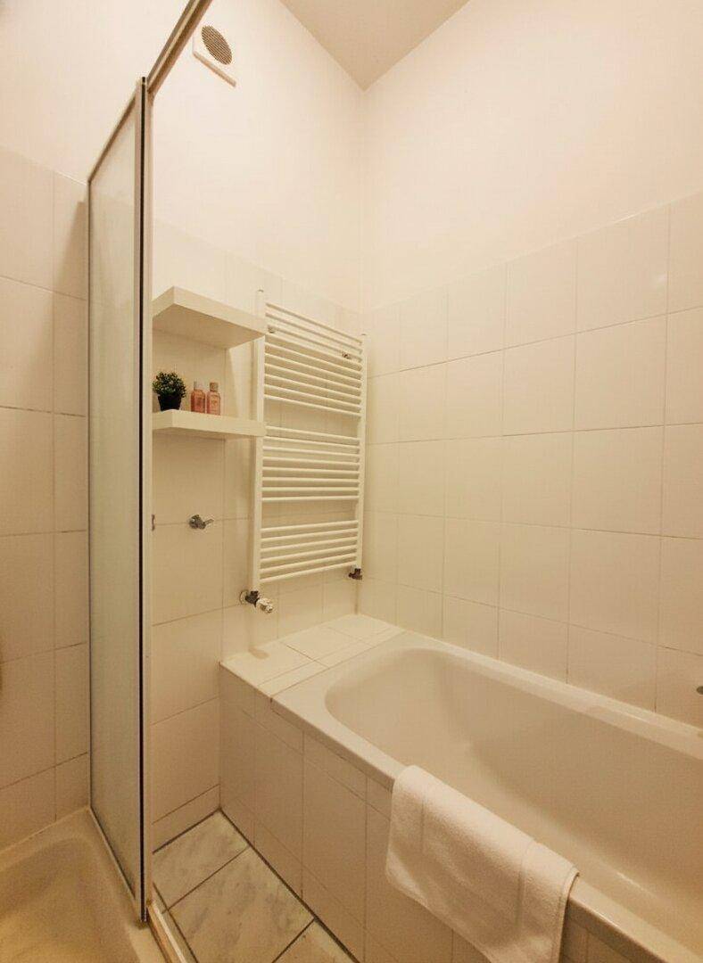 Helles Badezimmer mit Badewanne, Duschabtrennung und beheiztem Handtuchhalter, alles in Weiß gehalten.