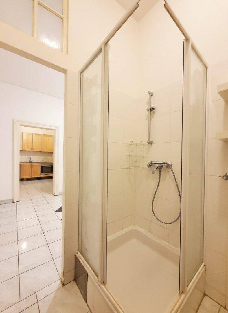 Duschkabine in einem Badezimmer mit Fliesenboden, das einen Blick in den angrenzenden Flur bietet.