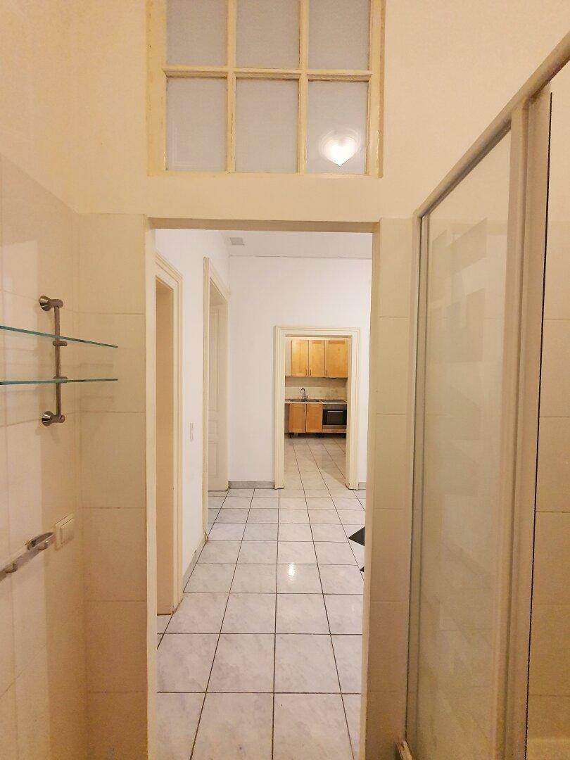 Badezimmer mit Duschkabine und Blick durch eine Tür in den gefliesten Flur und die Küche.