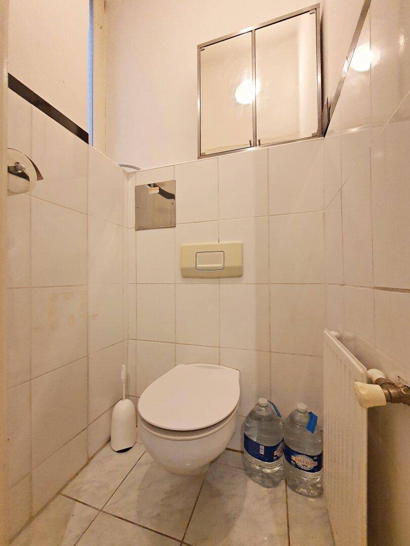 Kleines WC mit Wandtoilette und Fliesen an den Wänden, das funktional und sauber wirkt.