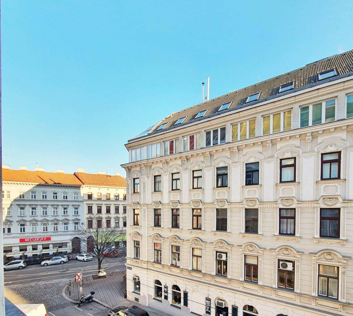Blick auf eine belebte Stadtstraße mit historischen Gebäuden und klarem blauem Himmel.