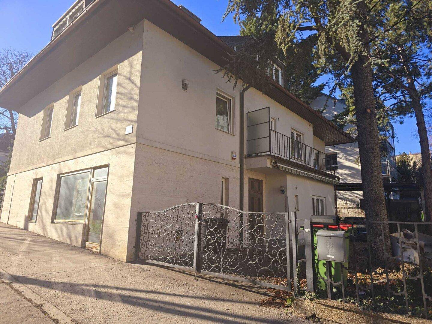Seitenansicht des Hauses mit Balkon, schmiedeeisernem Tor und viel Grün.
