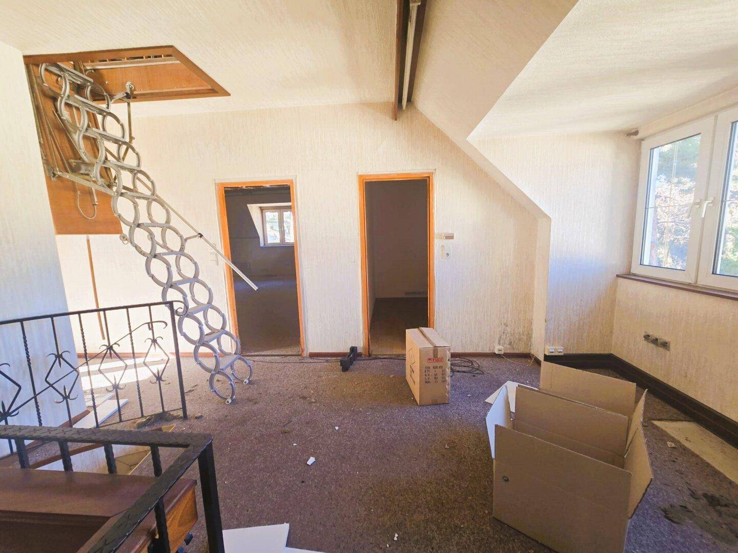 Dachgeschossraum mit ausziehbarer Treppe und Fenstern, bereit für den Ausbau.