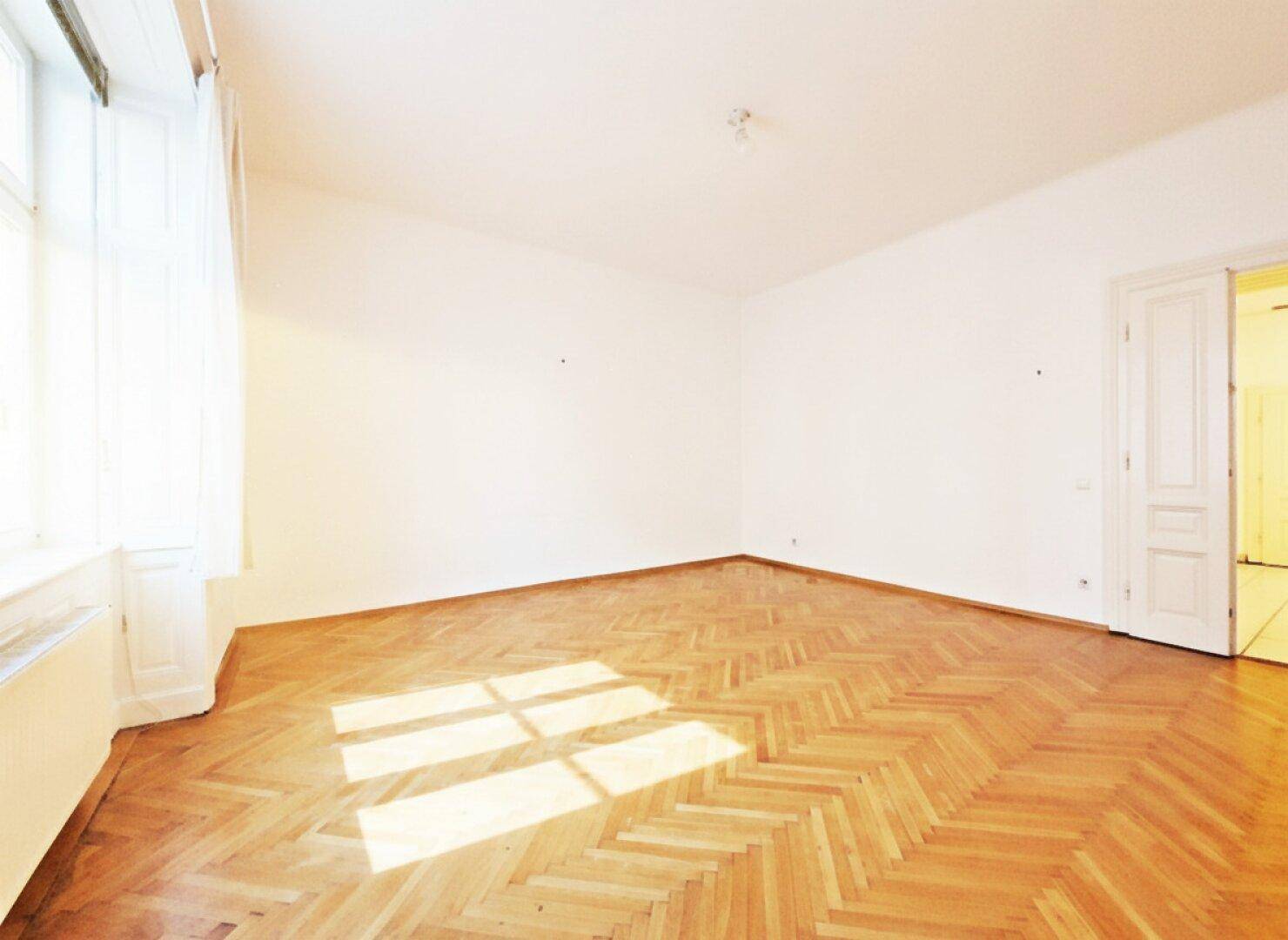 Heller Raum mit klassischem Fischgrätparkett und großen Fenstern, die den Raum mit Sonnenlicht füllen.