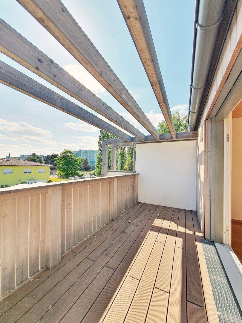 Balkon mit Holzbelag und Pergola-Struktur, bietet einen weiten Blick auf die Umgebung.