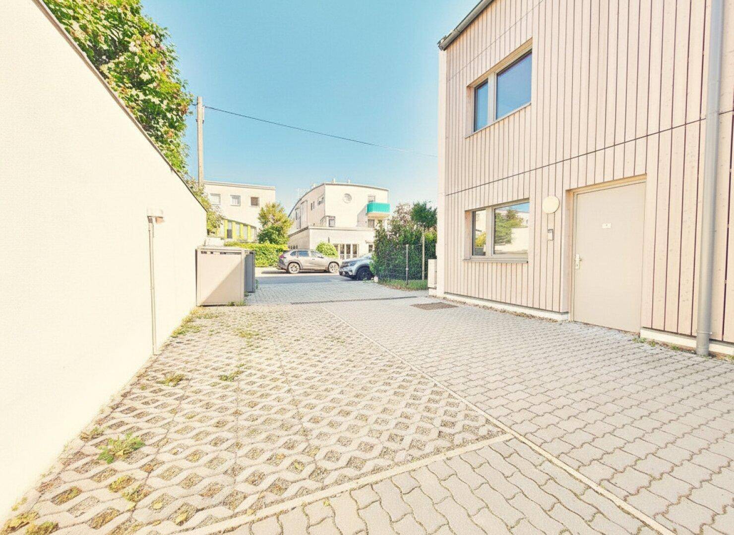 Seitenansicht des Gebäudes mit gepflastertem Parkplatz und Zufahrt.