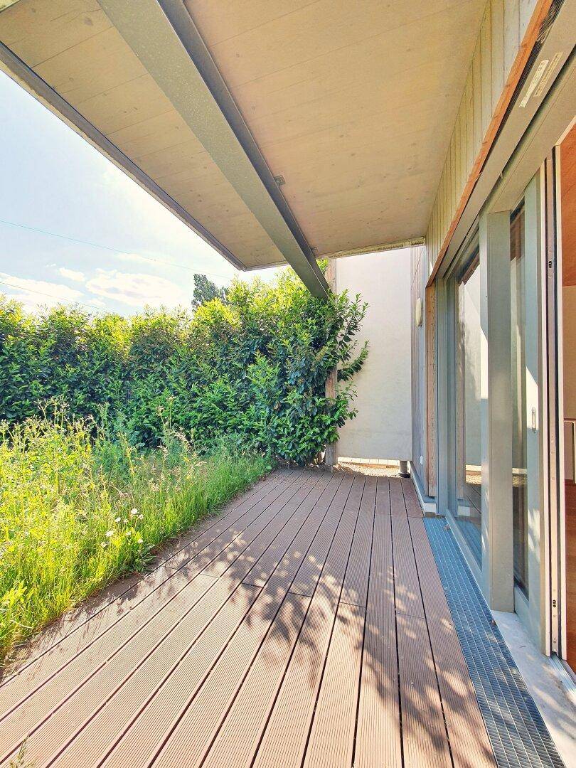 Überdachte Terrasse mit Holzbelag und Blick ins Grüne, ideal für Entspannung.