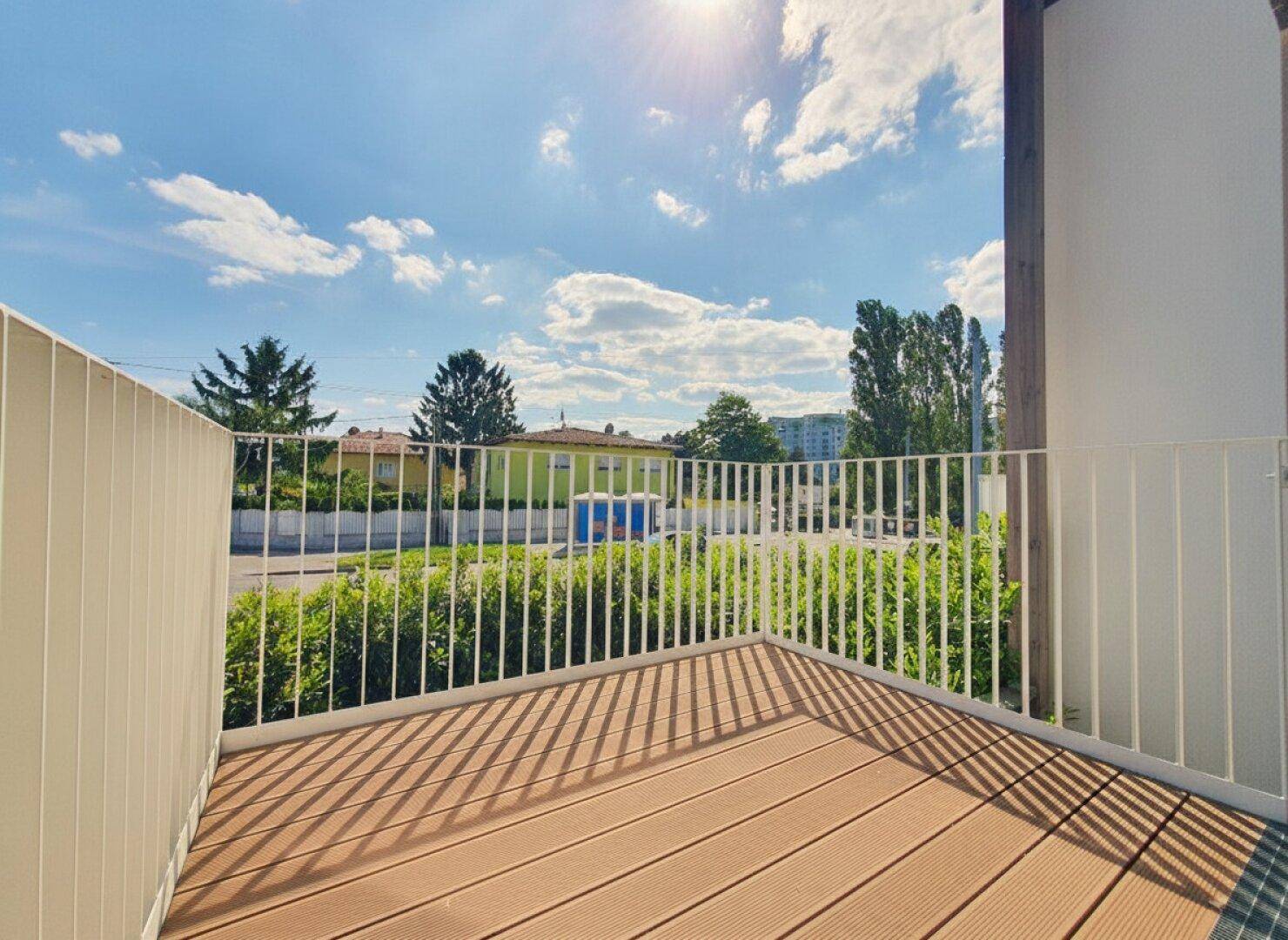Sonniger Balkon mit Holzbelag und weißem Geländer, bietet einen weiten Blick.