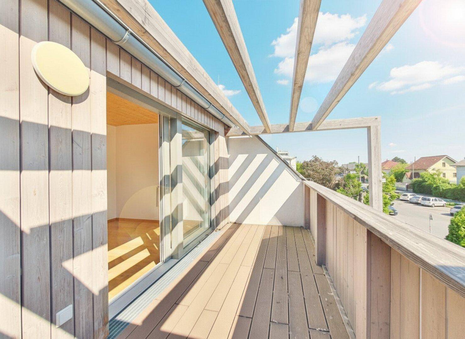 Sonniger Balkon mit Holzbelag und Pergola-Struktur, ideal für entspannte Stunden im Freien.