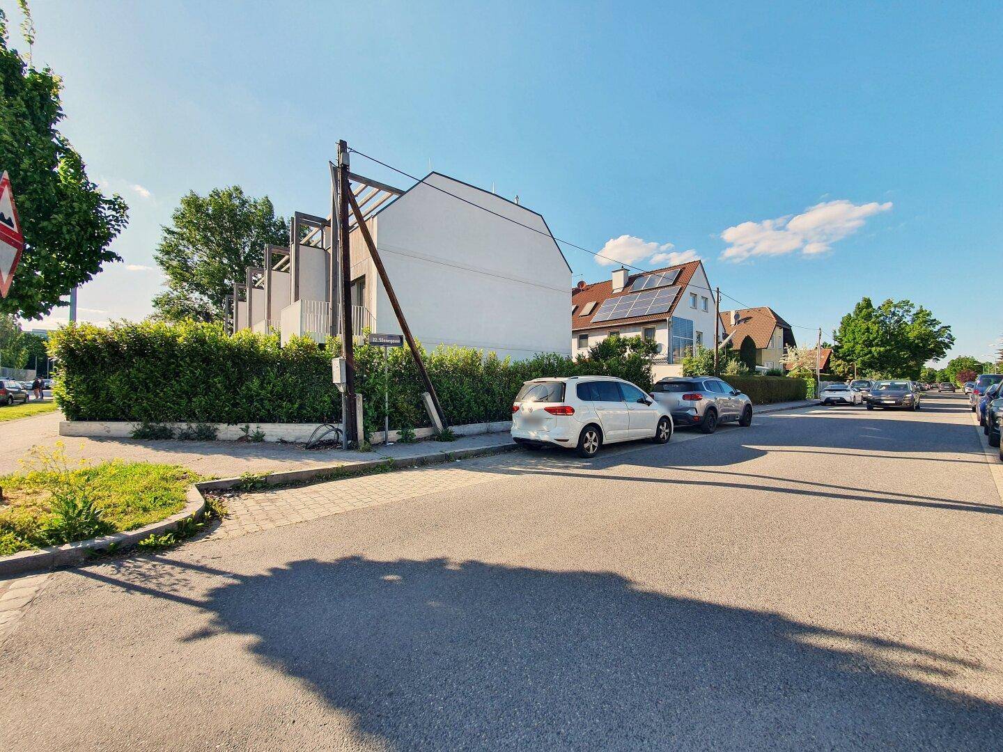 Blick auf die ruhige Wohnstraße mit parkenden Autos und umliegenden Häusern.