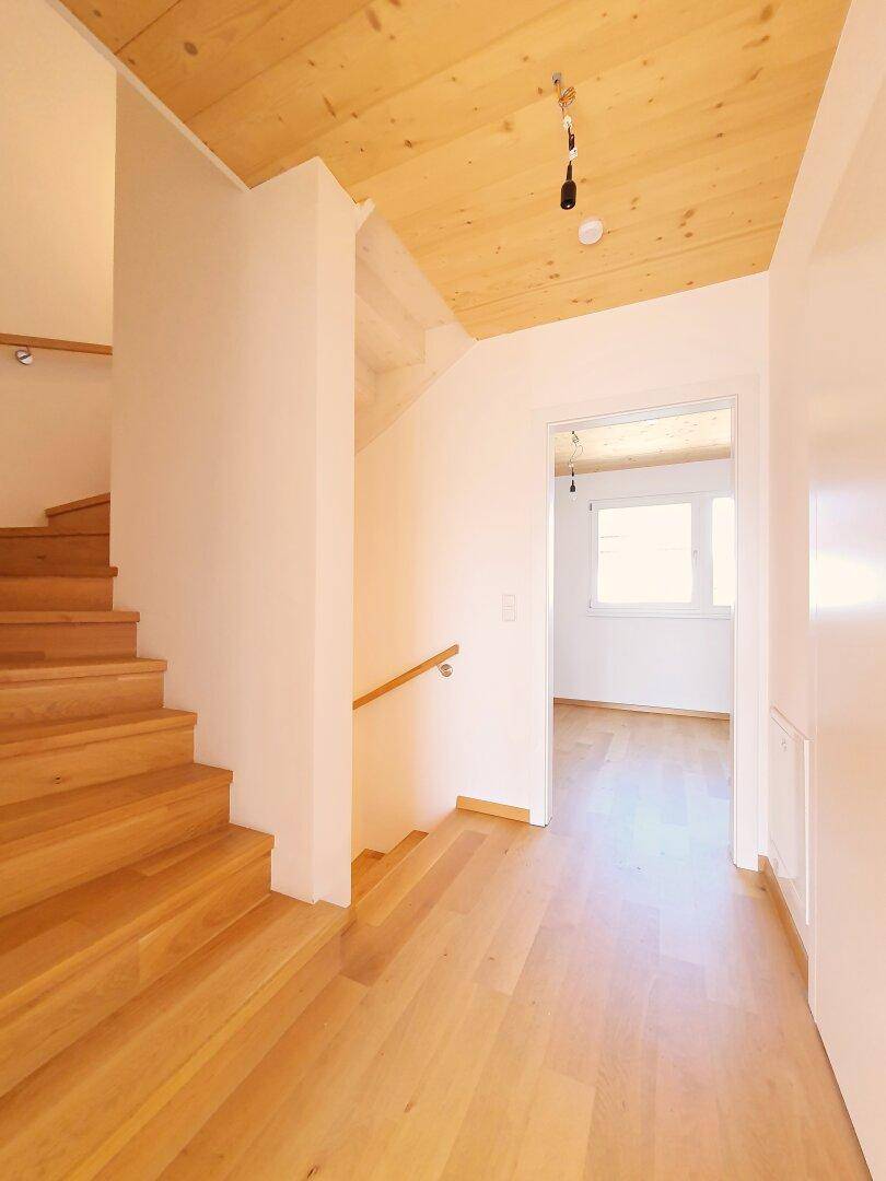 Heller Flur mit Holztreppe und Parkettboden, verbindet die verschiedenen Ebenen.