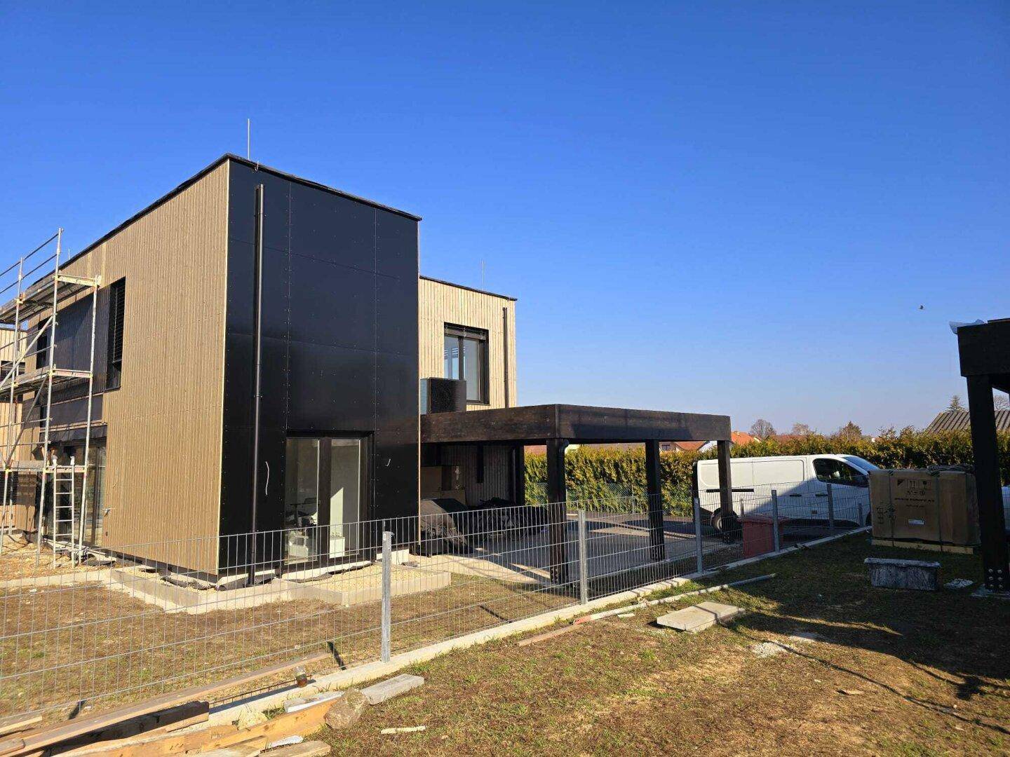 Neubau in Holzverkleidung mit schwarzer Fassade und Gerüst im Bauzustand.