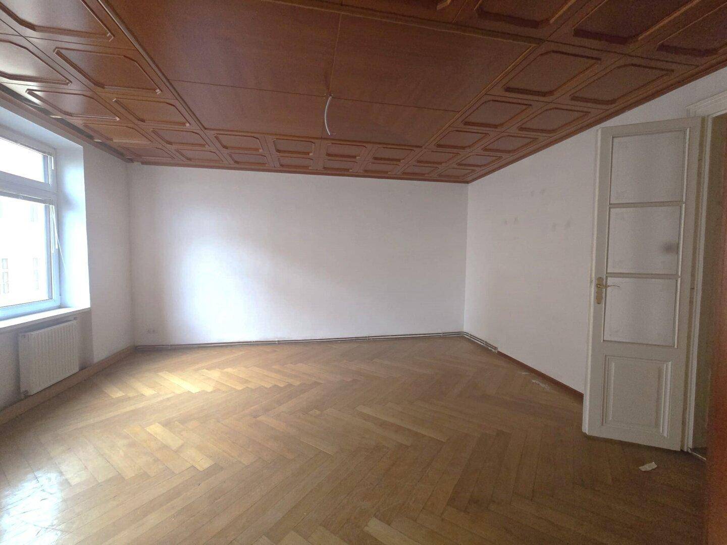Geräumiges Zimmer mit Fischgrätparkett und Holzpaneeldecke, ideal für Wohnzwecke.