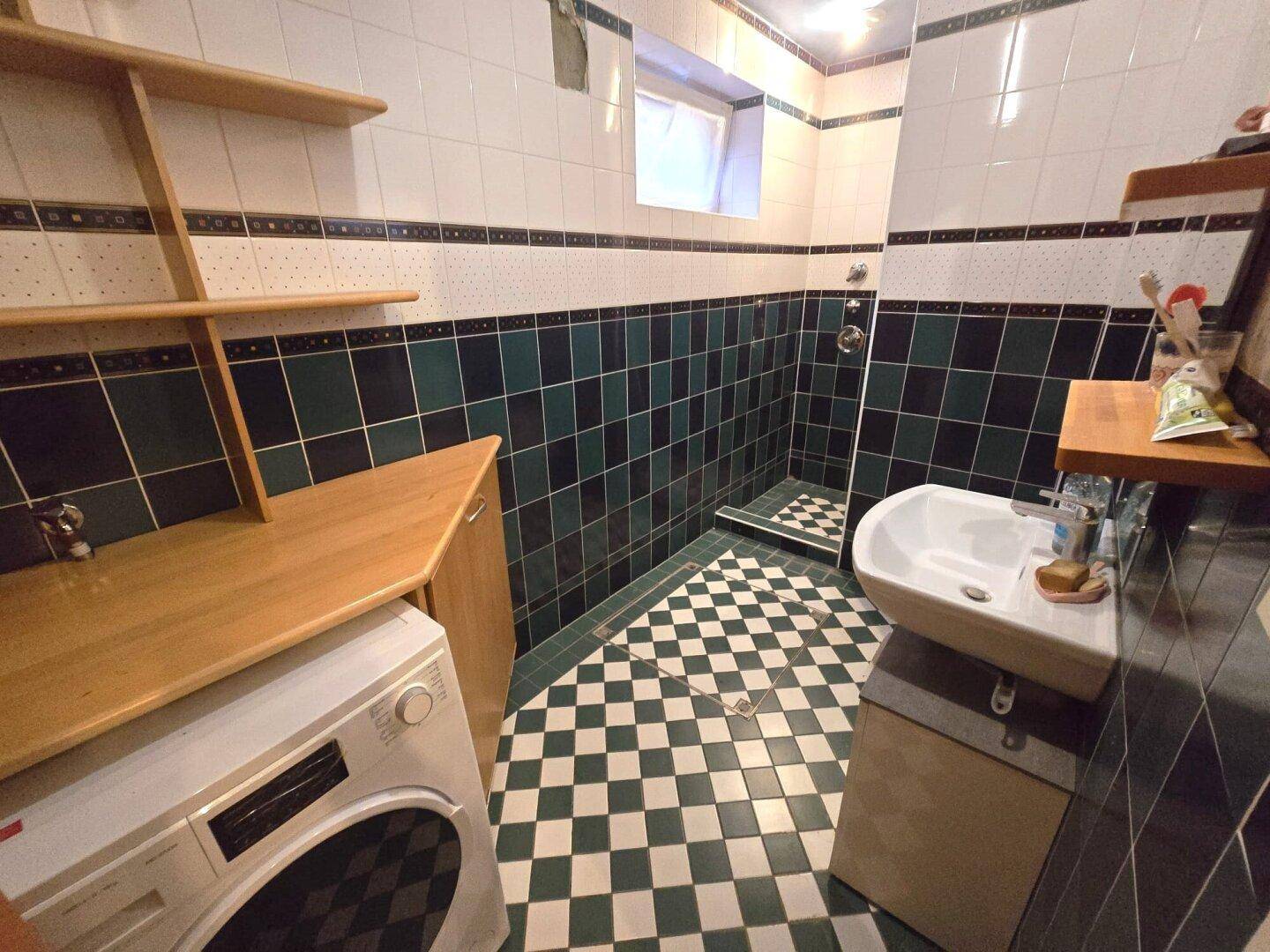 Modernes Badezimmer mit Dusche, Waschbecken und auffälligen grünen und weißen Fliesen.