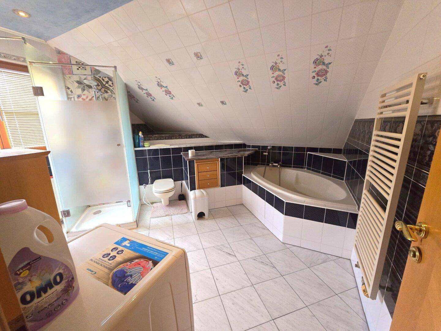 Badezimmer im Dachgeschoss mit Eckbadewanne, Dusche und Waschmaschine.
